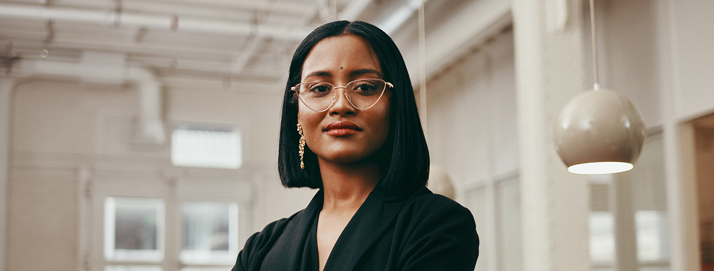 A woman with short hair and glasses wearing a black suit and folding her arms - International Diversity Merit Scholarship (1440x548)