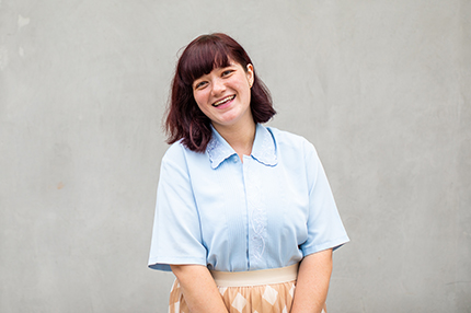 A young female international student with red hair and a a light blue blouse, smiling towards camera (430x286).