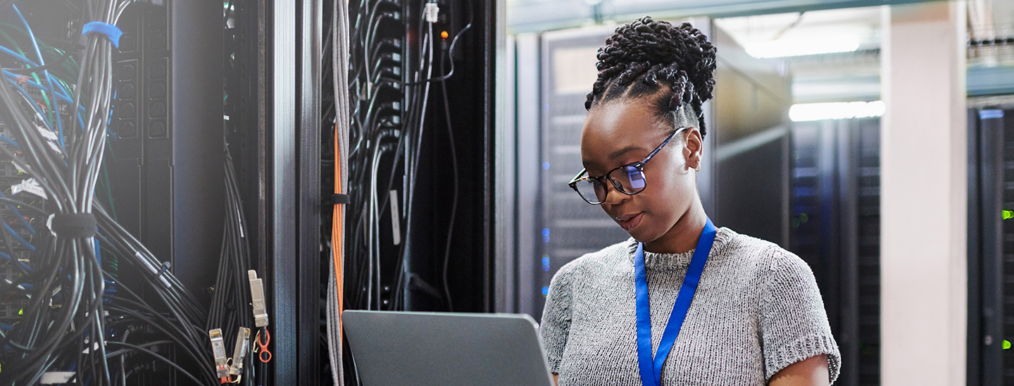 A young female Bachelor of Information Technology student standing and using a laptop (1440x548)