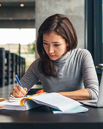 A female Bachelor of Accounting student sitting at a desk and writing in a notebook (400x500).