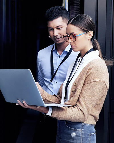 Two Bachelor of Information Technology students standing together and looking towards a laptop screen in one student's hands (400x500).