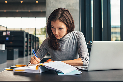 A young female Bachelor of Accounting student working with a pen and notebook, with an open laptop in front of her (430x286)