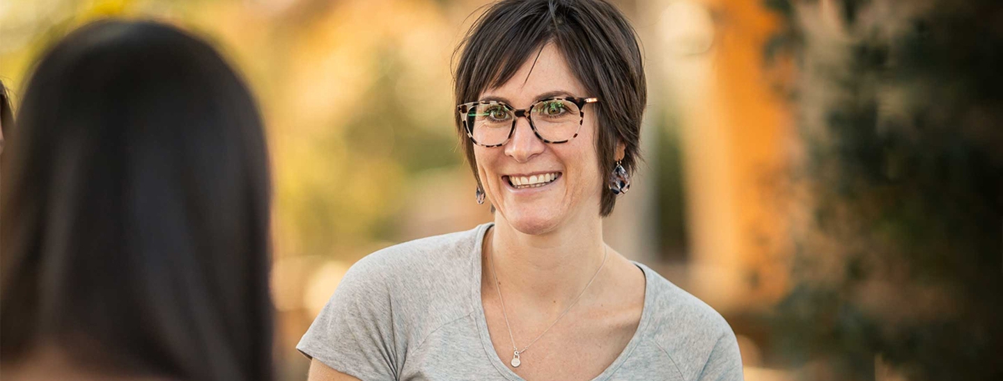 A women with short brown hair and glasses, facing towards another woman in the foreground