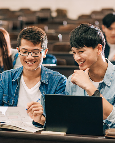 Two male Master of Business Data Analytics students sitting together in a lecture hall and looking towards a piece of paper in one student's hands (400x500).