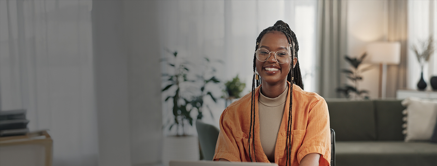 A young female Master of Health Professional Practice student sitting in a room in front of a laptop and smiling towards camera (1440x548)