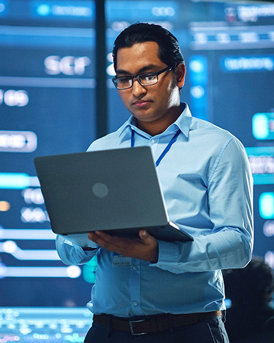 A male Master of Information Technology student standing with an open laptop in his hands (400x500).