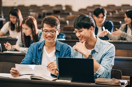 Two male Master of Business Data Analytics students sitting at a desk in a lecture theatre, looking at a piece of paper in one student's hand