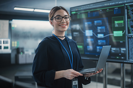 A female Master of Professional Information Technology student wearing glasses and standing with a laptop in her hands (430x286)