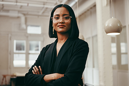 A female Master of Professional Accounting student wearing glasses and standing with her arms folded in a classroom (430x286)