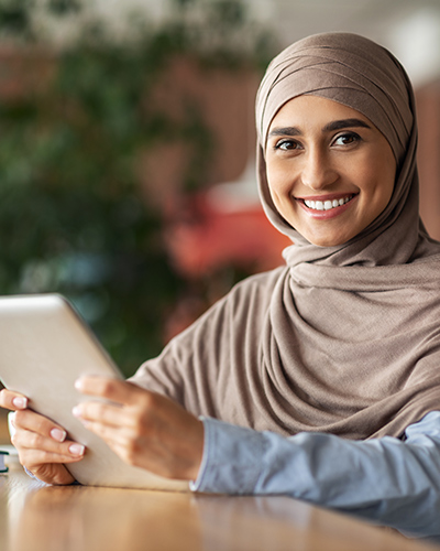 A female Master of Social Work (Qualifying) student sitting at a desk with a tablet in her hands and smiling towards camera (400x500).