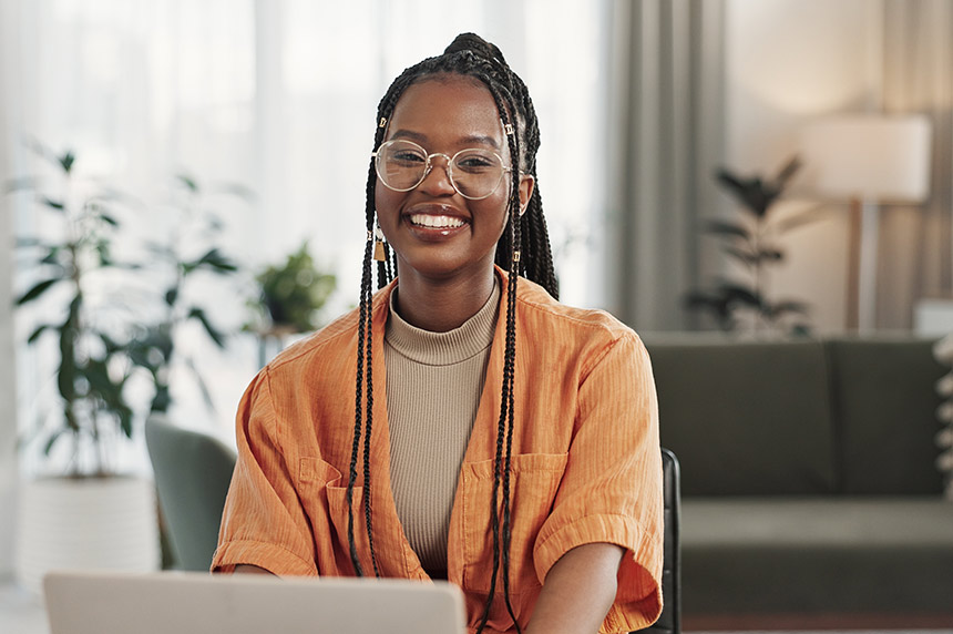 A young female Master of Health Professional Practice student sitting in a room in front of a laptop and smiling towards camera (860x572)