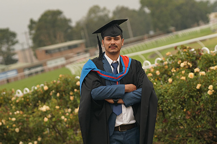 Master of Information Technology graduate Santosh standing at his graduation ceremony with his arms folded and wearing a mortarboard