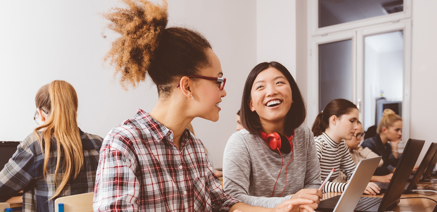 Two female students working together at a desk and smiling