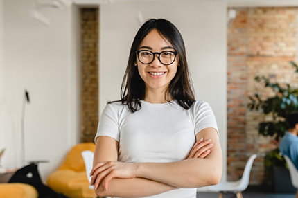 A female student wearing glasses and standing with her arms folded in an office space - 430x286