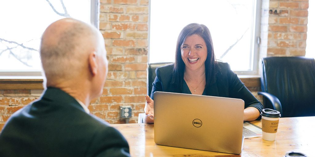 A woman sitting at a desk in front of an open Dell laptop, smiling towards a man sitting on the other side of the table - Certified Practising Accountant (CPA)